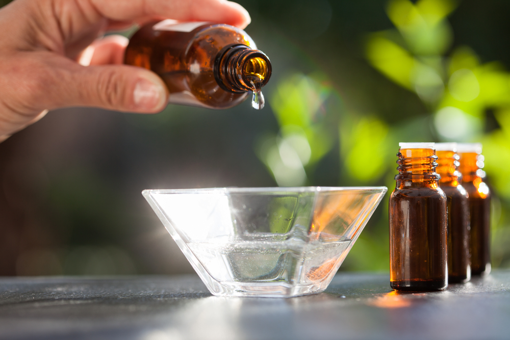 Hand pouring essential oil into a glass bowl outdoors